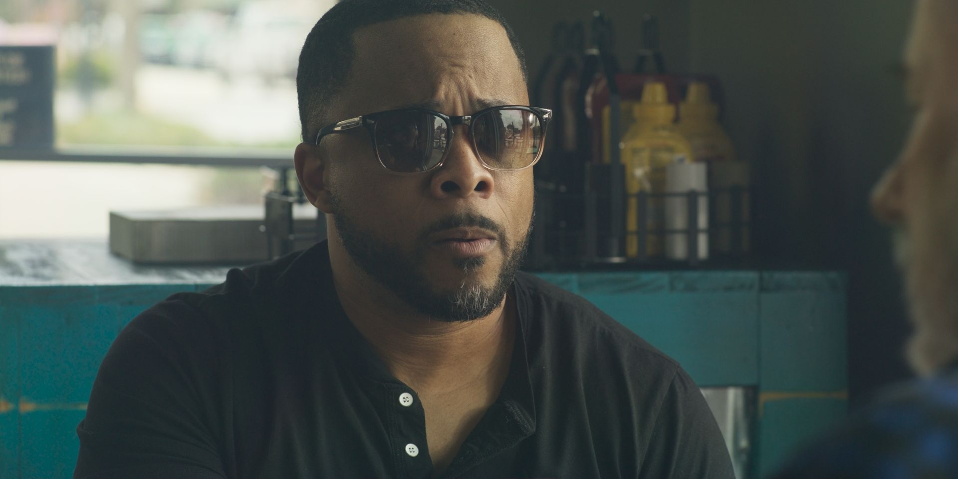 Still from Fifthe Dimension Studios: a man in sunglasses at a diner counter, teal walls behind him